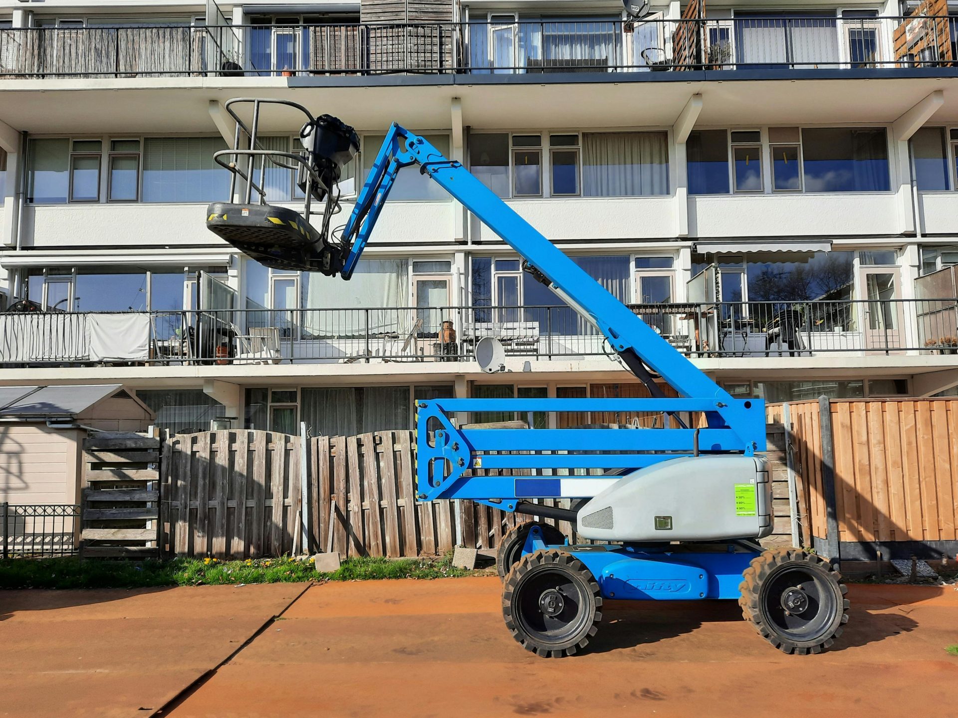 Un montacargas azul se ve frente a un edificio residencial bajo la intensa luz del sol en los Países Bajos.